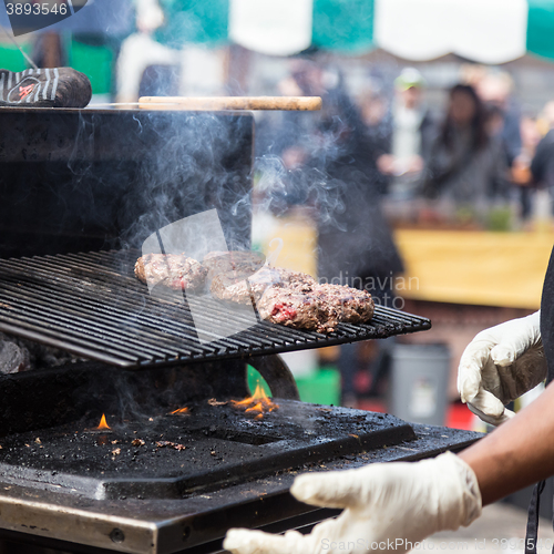 Image of Beef burgers being grilled on food stall grill.