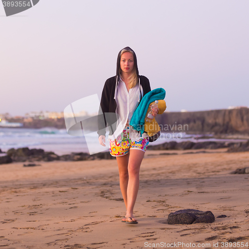 Image of Sporty woman walking on sandy beach in sunset.