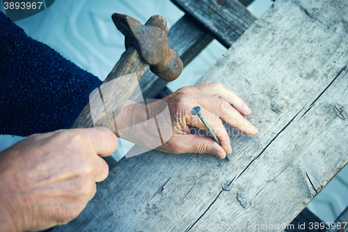 Image of Closeup of mature man hands nails with old hammer 