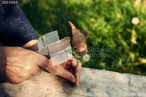 Image of Closeup of mature man hands nails with old hammer 