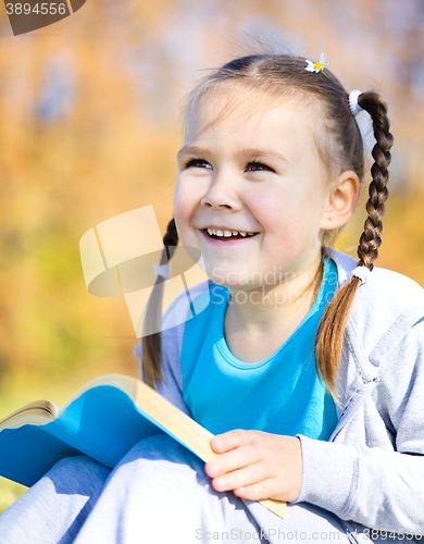 Image of Little girl is reading a book outdoors