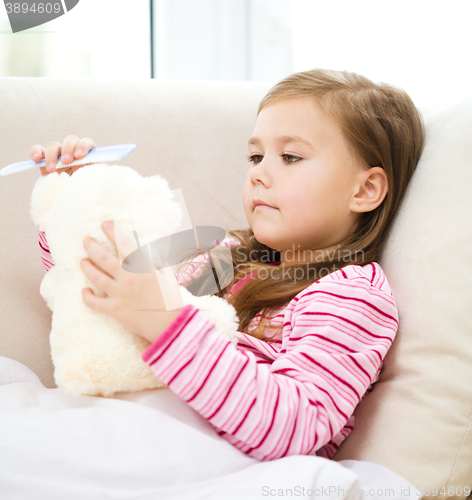Image of Little girl is combing her teddy bear