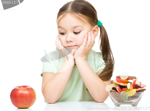Image of Little girl choosing between apples and sweets