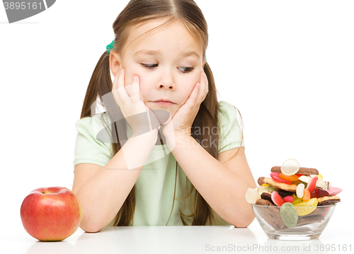 Image of Little girl choosing between apples and sweets