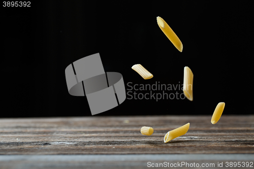 Image of Falling penne pasta. Flying yellow raw macaroni over black background.