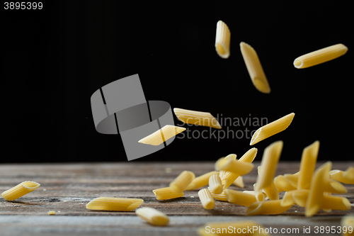 Image of Falling penne pasta. Flying yellow raw macaroni over black background.