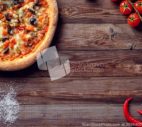 Image of Italian pizza with tomatoes on a wooden table, top view.