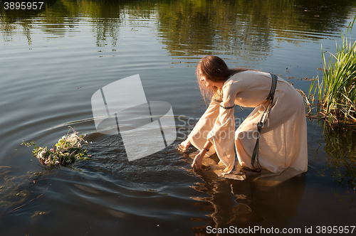 Image of Attractive girl lowers wreath in water