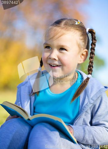 Image of Little girl is reading a book outdoors