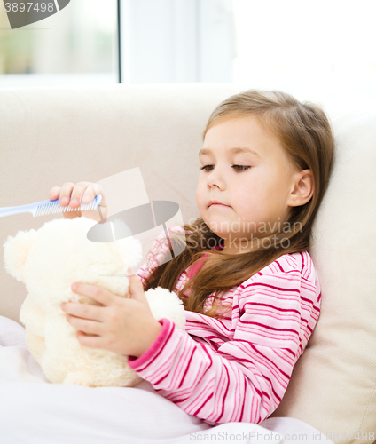 Image of Little girl is brushing her teddy bear