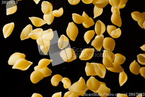 Image of Falling conchiglie pasta. Flying yellow raw macaroni over black background.