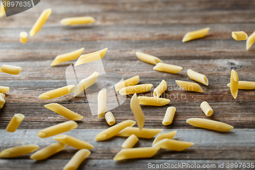 Image of Falling penne pasta. Flying yellow raw macaroni over black background.