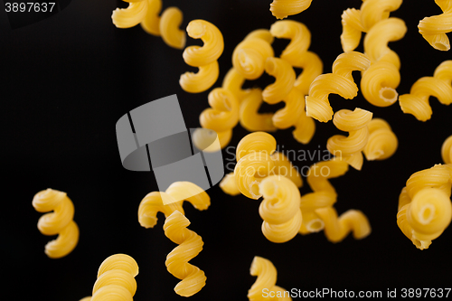 Image of Falling cavatappi pasta. Flying yellow raw macaroni over black background. 