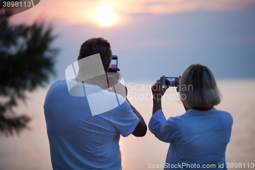 Image of Back view of couple taking photos of sunset