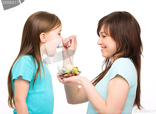 Image of Mother is feeding her daughter with fruit salad