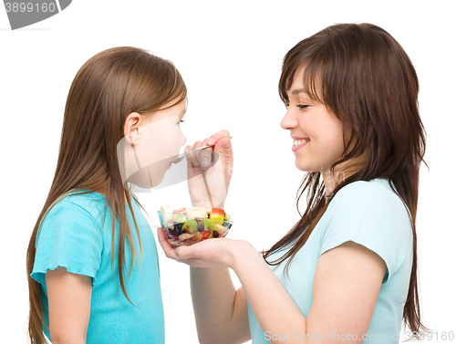 Image of Mother is feeding her daughter with fruit salad