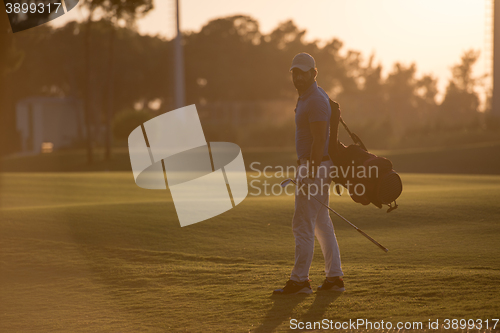 Image of golfer  walking and carrying golf  bag at beautiful sunset