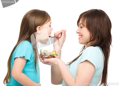 Image of Mother is feeding her daughter with fruit salad