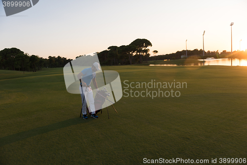 Image of golfer  walking and carrying golf  bag at beautiful sunset