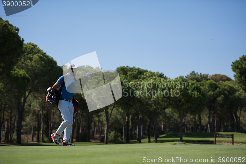 Image of golf player walking and carrying bag