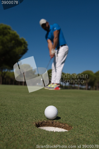 Image of golf player hitting shot, ball on edge of hole