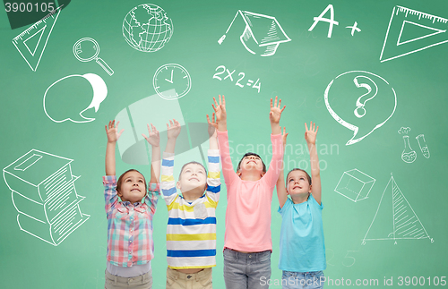 Image of happy children raising hands over green blackboard