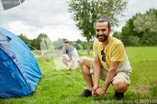 Image of smiling friends setting up tent outdoors