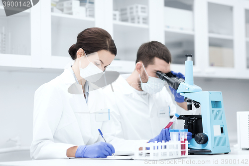 Image of scientists with clipboard and microscope in lab