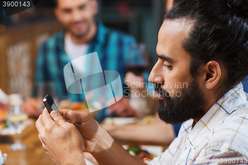 Image of man with smartphone and friends at restaurant