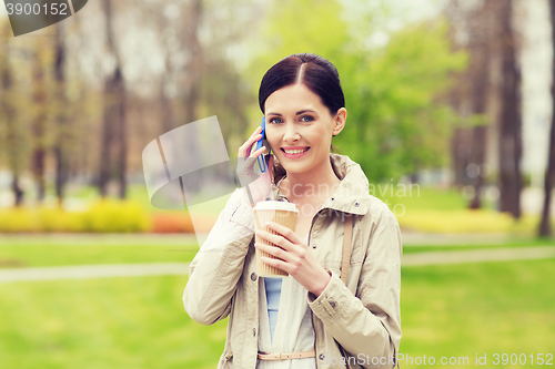 Image of smiling woman with smartphone and coffee in park