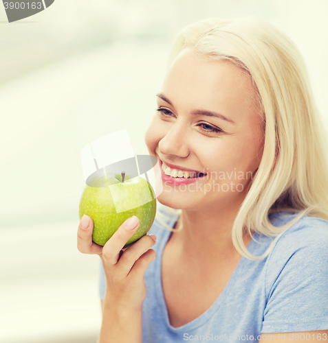 Image of happy woman eating green apple at home