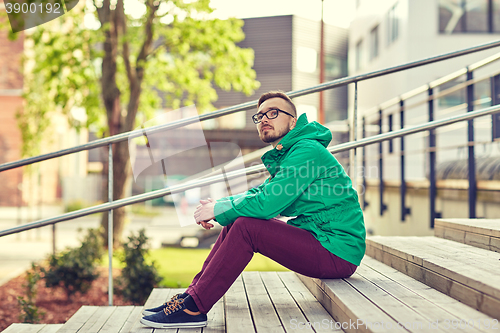 Image of happy young hipster man sitting on stairs in city