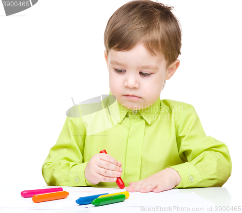 Image of Little boy is drawing on white paper using crayon