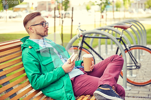 Image of happy young hipster man with coffee and sandwich