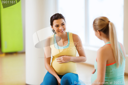 Image of two happy pregnant women sitting on balls in gym