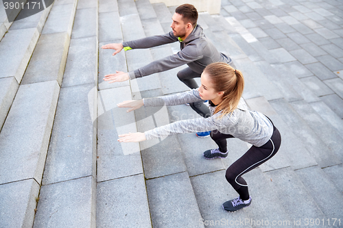 Image of couple doing squats on city street stairs