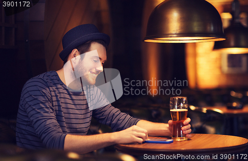 Image of man with smartphone and beer texting at bar