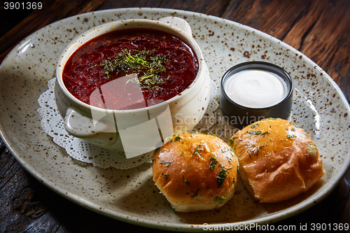 Image of red borscht with sour cream, wild garlic, bread on a wooden background