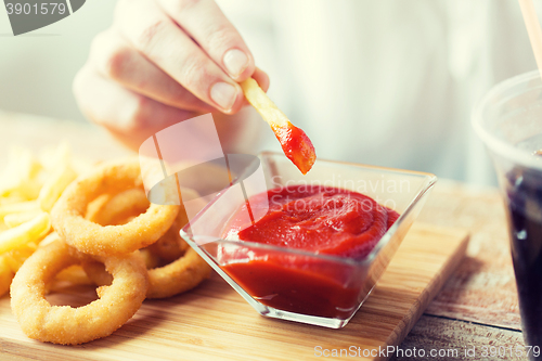 Image of close up of hand dipping french fries into ketchup