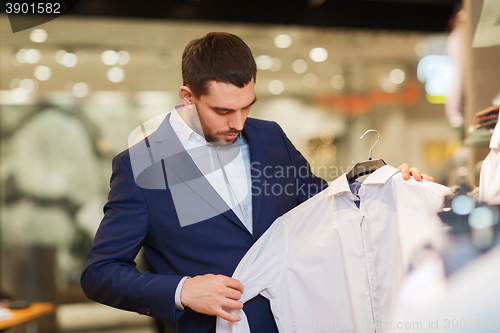 Image of happy young man choosing clothes in clothing store