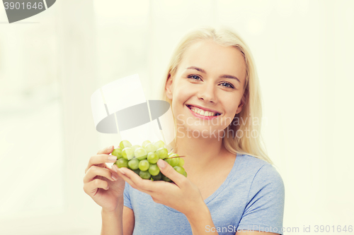 Image of happy woman eating grapes at home