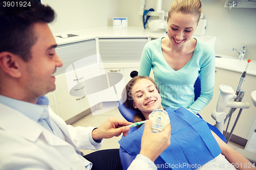 Image of happy dentist showing toothbrush to patient girl