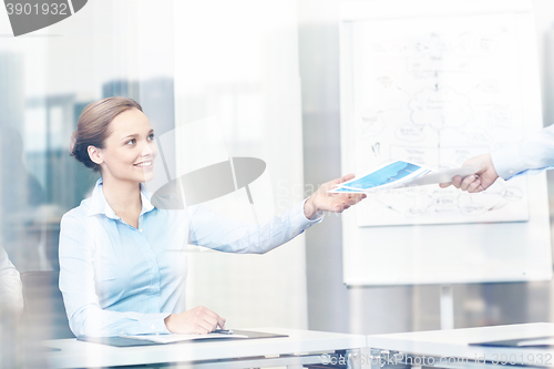 Image of businesswoman taking papers from someone in office