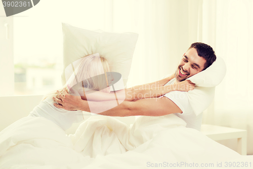 Image of happy couple having pillow fight in bed at home