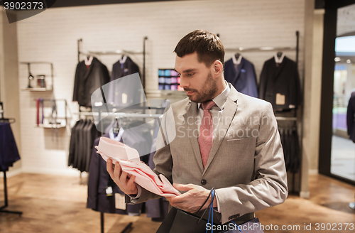 Image of man with bags choosing shirt in clothing store