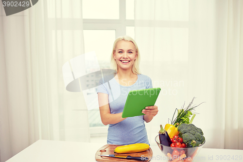 Image of smiling young woman with tablet pc cooking at home