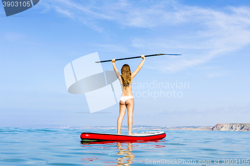 Image of A beautiful and happy woman with arms up and learning paddle-sur