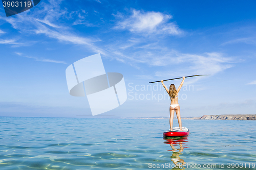 Image of A beautiful and happy woman with arms up and learning paddle-sur