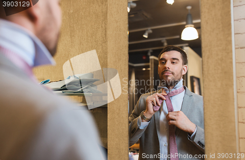 Image of man tying tie on at mirror in clothing store