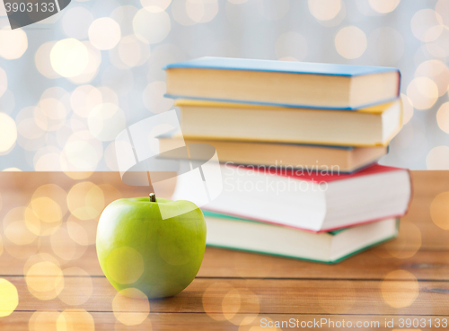Image of close up of books and green apple on wooden table